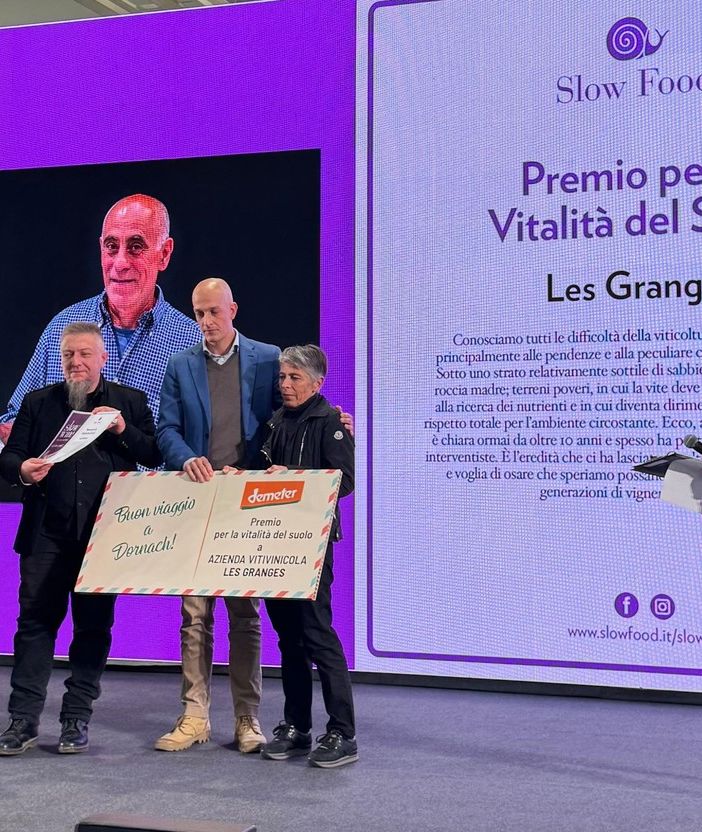 Liana Grange riceve il premio sul palco di Slow Wine; sullo sfondo, il volto di Gualtiero Crea