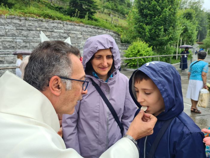 Don Isidoro Mercuri Giovinazzo offre la comunione a un bimbo sul sagrato di Lourdes