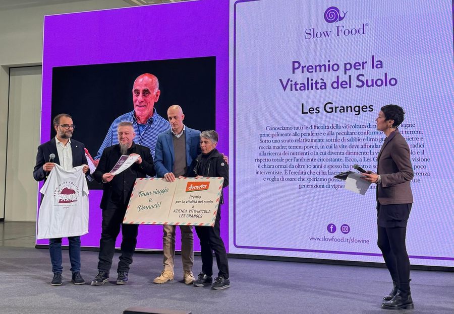Liana Grange riceve il premio sul palco di Slow Wine; sullo sfondo, il volto di Gualtiero Crea Liana Grange riceve il premio sul palco di Slow Wine; sullo sfondo, il volto di Gualtiero Crea