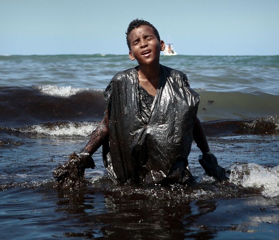 Un ragazzo emerge dalle acque invase dal petrolio davanti alla spiaggia di Itapuama, in Brasile (fotografia di Leo Malafaia)