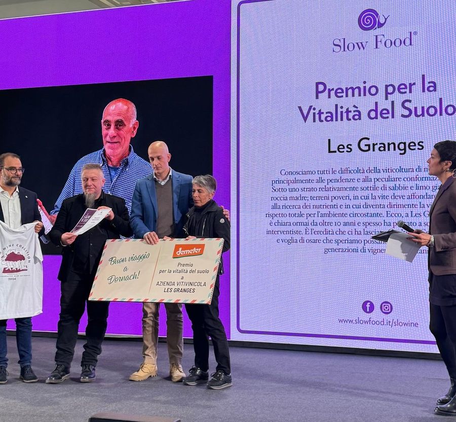 Liana Grange riceve il premio sul palco di Slow Wine; sullo sfondo, il volto di Gualtiero Crea