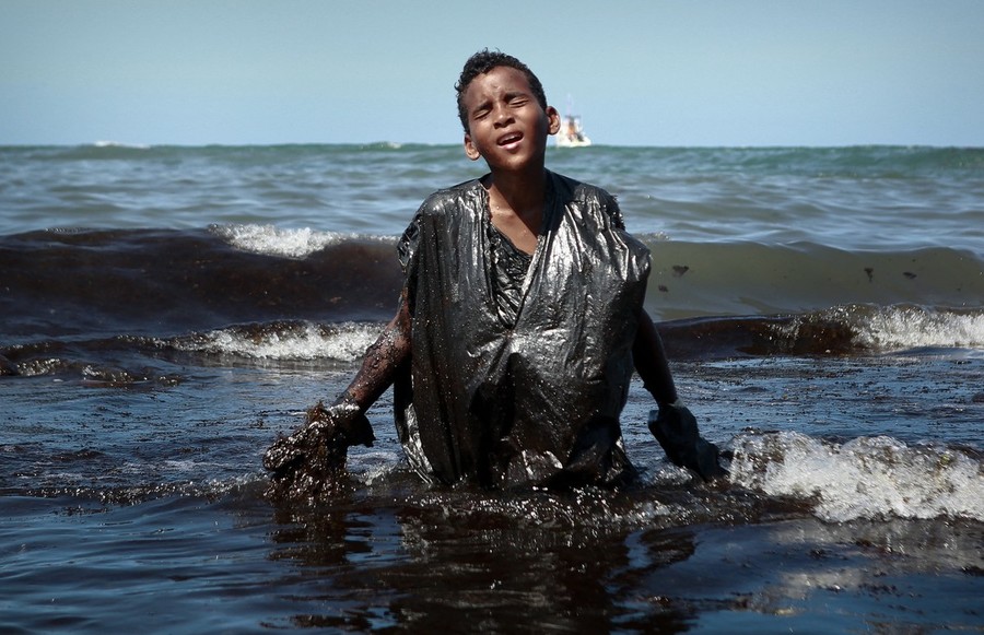Un ragazzo emerge dalle acque invase dal petrolio davanti alla spiaggia di Itapuama, in Brasile (fotografia di Leo Malafaia)
