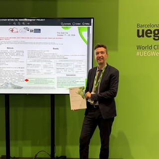 ll dottor Stefano Okolicsanyi alla UEG Week 2026 di Barcellona accanto al poster della ricerca del progetto 5000genomi@VdA, con l'attestato del Best Abstract Presentation Prize